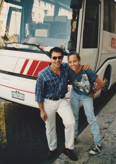 Two smiling people, one older and one younger, with arms around each other in front of a Globus tour bus