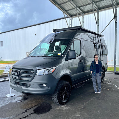Blue Dulac standing next to a Mercedes Benz Sprinter 2022 Stealth MODE 4x4 Storyteller Overland on pickup day