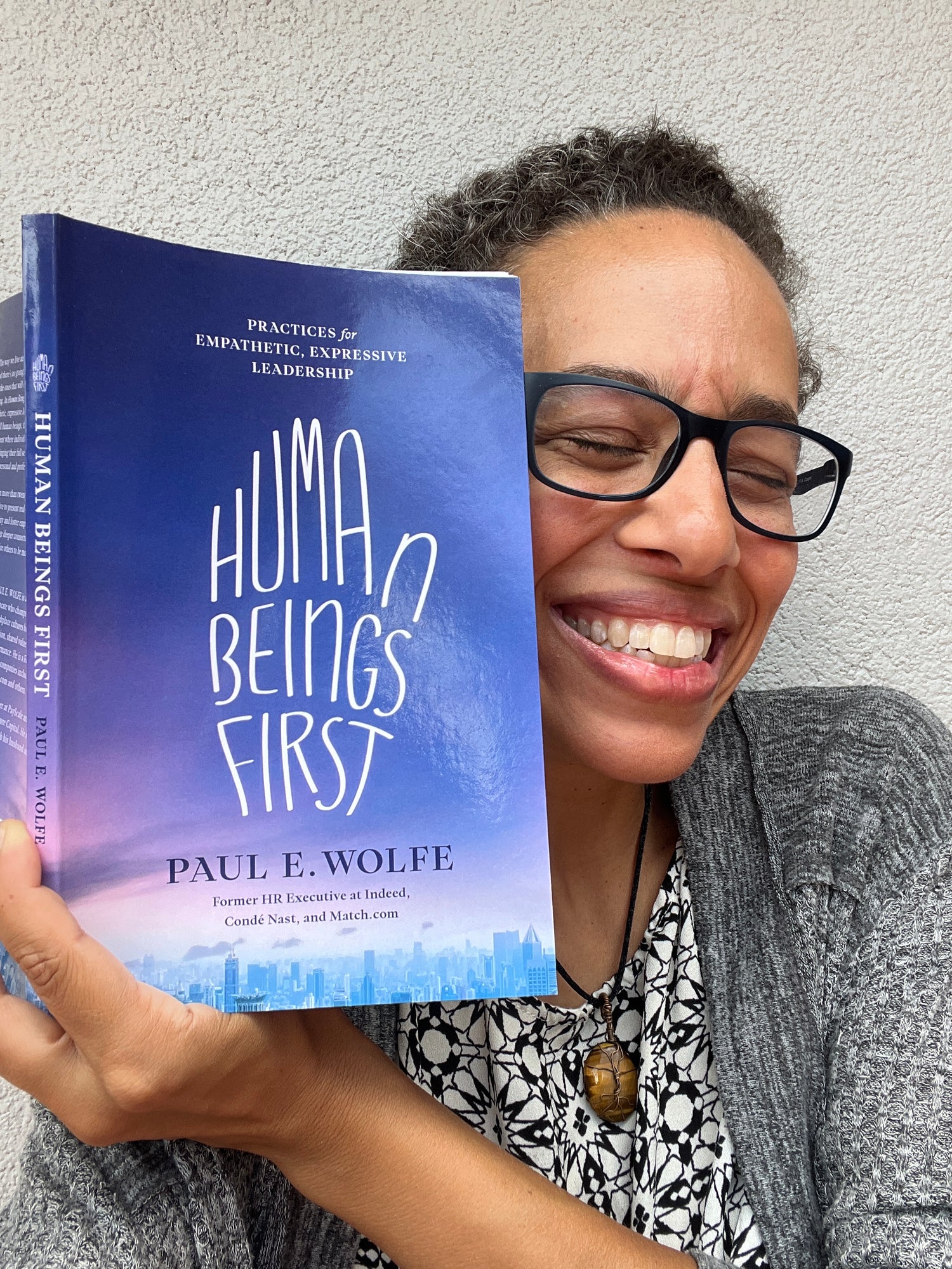 Person grinning holding a book titled 'Human Beings First' by Paul E. Wolfe against a neutral background