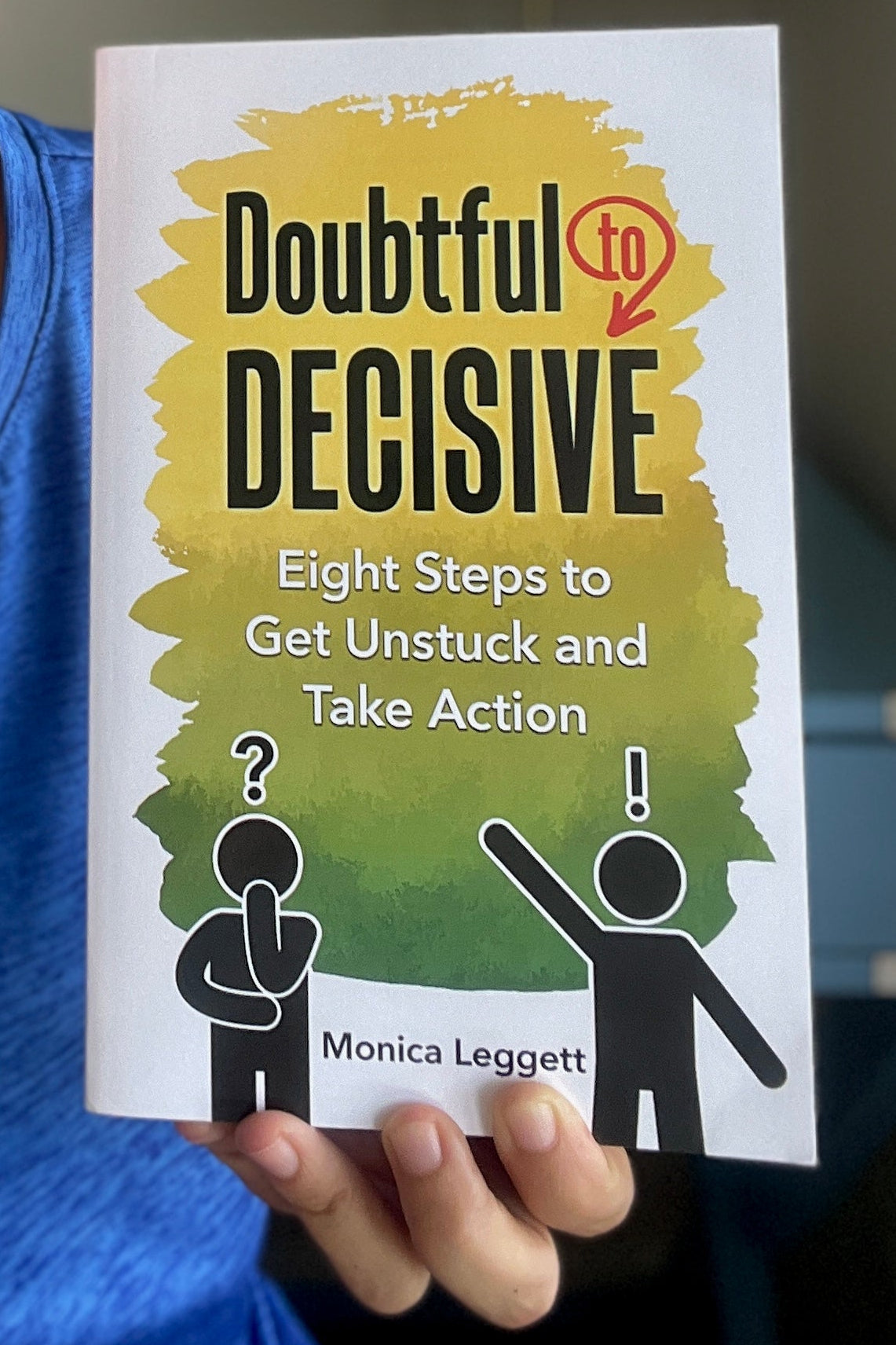 Hand holding a book titled 'Doubtful Decisive: Eight Steps to Get Unstuck and Take Action' by Monica Leggett