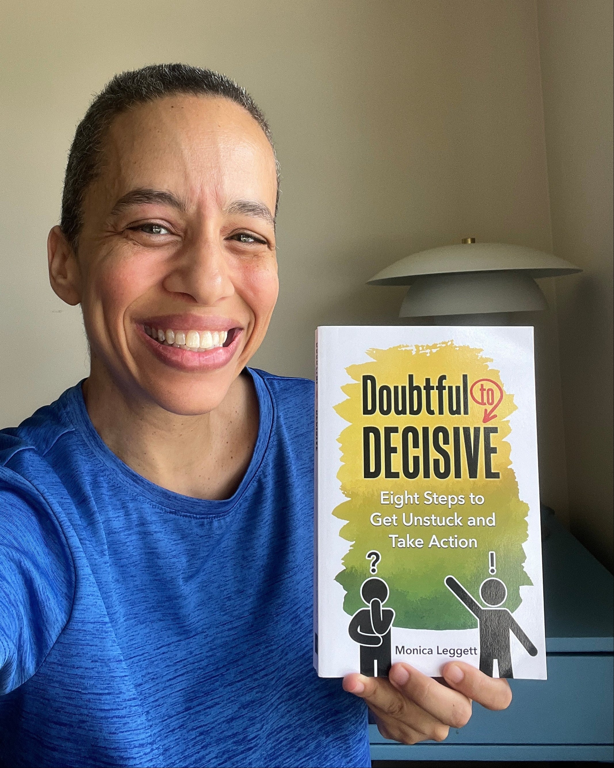 Person ginning holding a book titled 'Doubtful Decisive: Eight Steps to Get Unstuck and Take Action' by Monica Leggett against a plain background